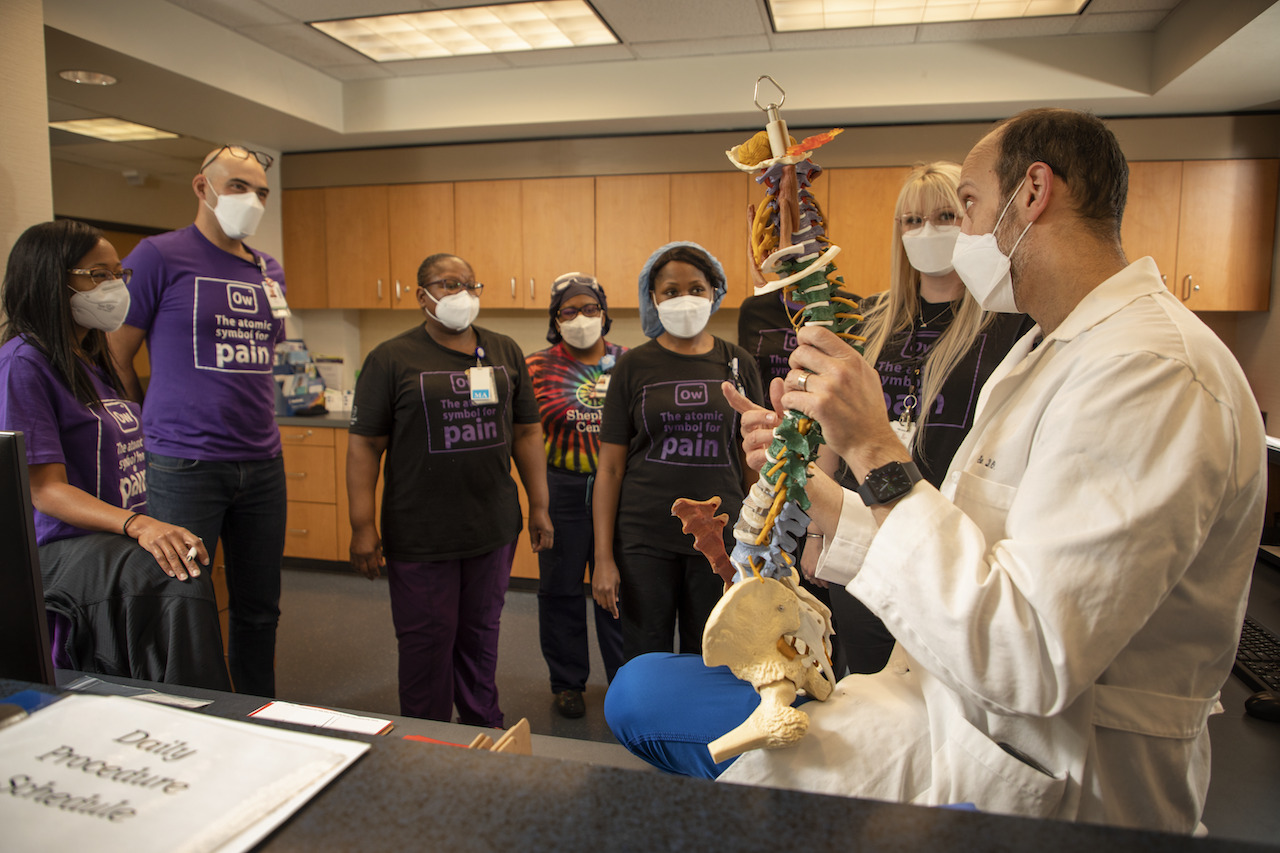A group of people watching a doctor teach. The doctor is holding an artificial spine.