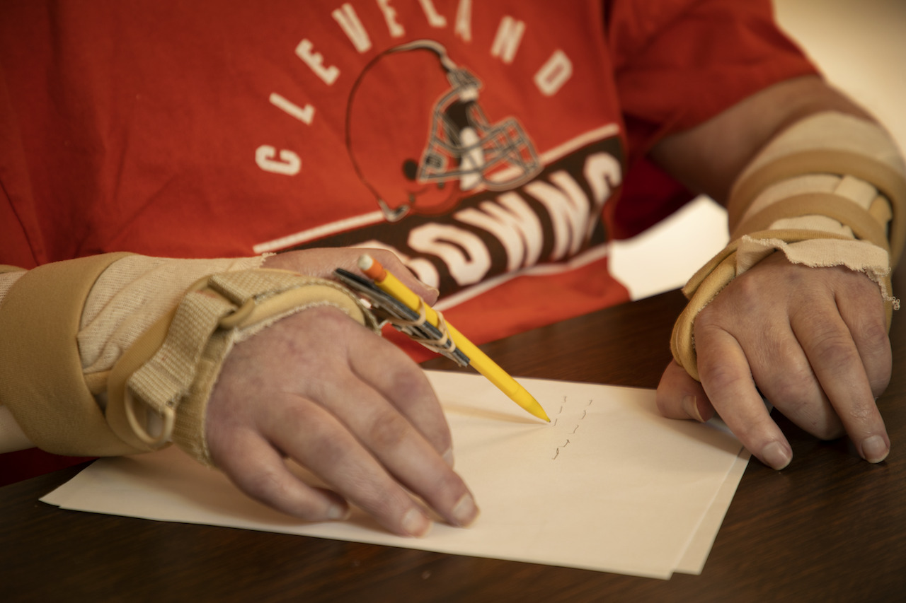 Man writing on paper with an adaptive handwriting tool.