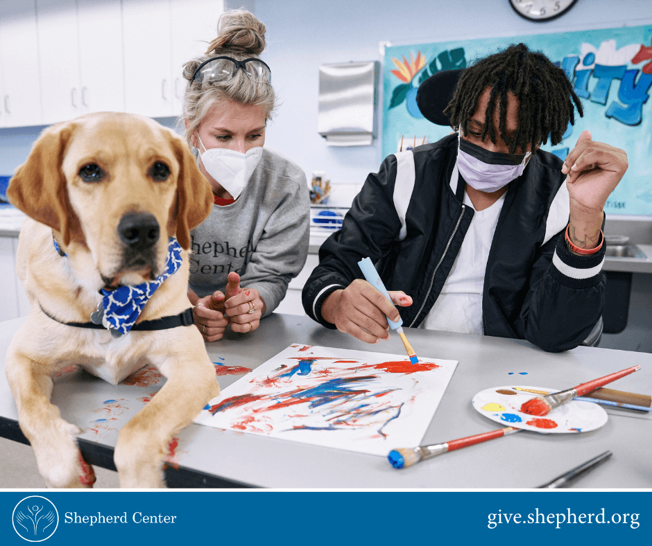 Shepherd patient painting a photo with Shepherd staff member and therapy dog.