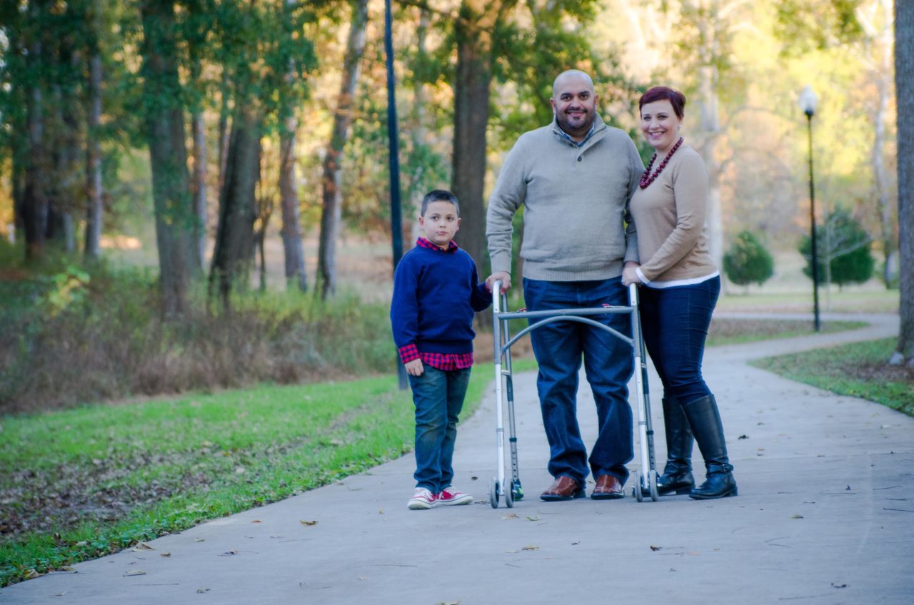 Father, mother, and son walking in a park; father is using a walker