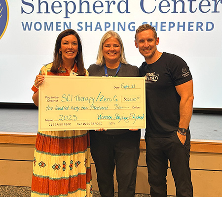 A member from Women Shaping Shepherd presents a check to the SCI Therapy team for $262,000.