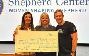 A member from Women Shaping Shepherd presents a check to the SCI Therapy team for $262,000.