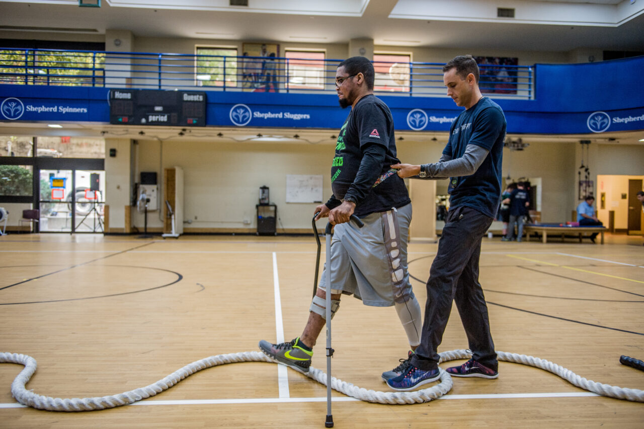 ports therapist helps patient as they practice balance and gait walking in the Shepherd Center gym.