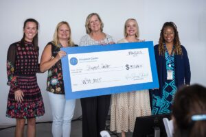 Five women stand together holding a large ceremonial check for $320,101 made out to Shepherd Center.